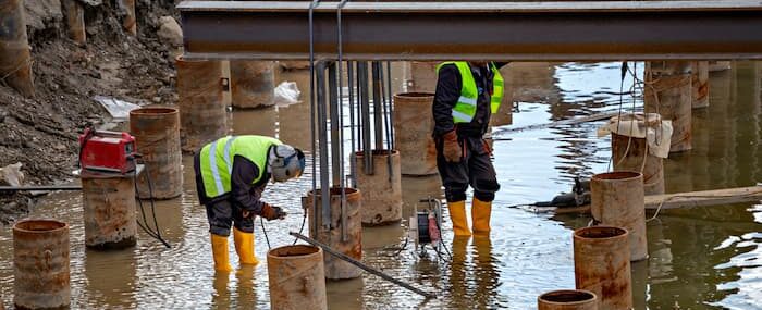 Construction workers dangerously welding and grinding under wet conditions
