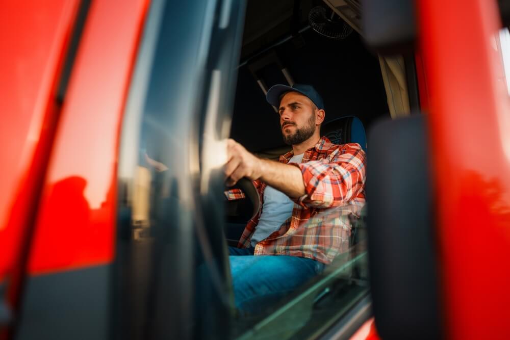 Truck driver operating red semi-truck — representing Truck Driver Workers’ Compensation in NC.