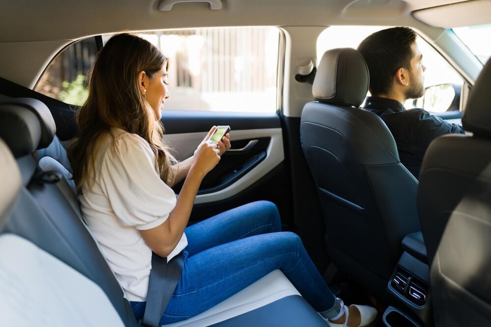 Female passenger using phone in backseat of rideshare vehicle with driver — Rideshare Accident Lawyer in Summerfield, NC
