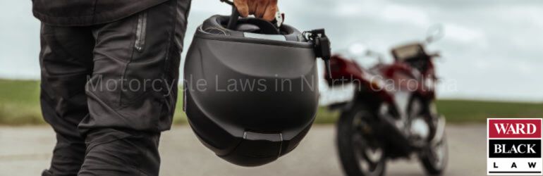 Motorcyclist holding helmet with motorcycle in background – North Carolina motorcycle safety laws